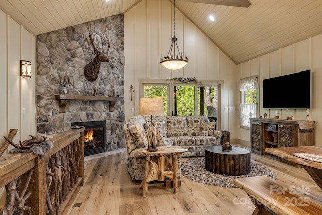living area featuring wooden ceiling, high vaulted ceiling, light wood-type flooring, and a stone fireplace