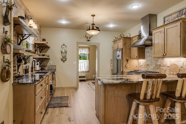 kitchen featuring wall chimney range hood, open shelves, a sink, freestanding refrigerator, and a peninsula