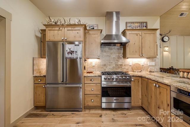 kitchen featuring wall chimney range hood, light stone countertops, decorative backsplash, premium appliances, and visible vents