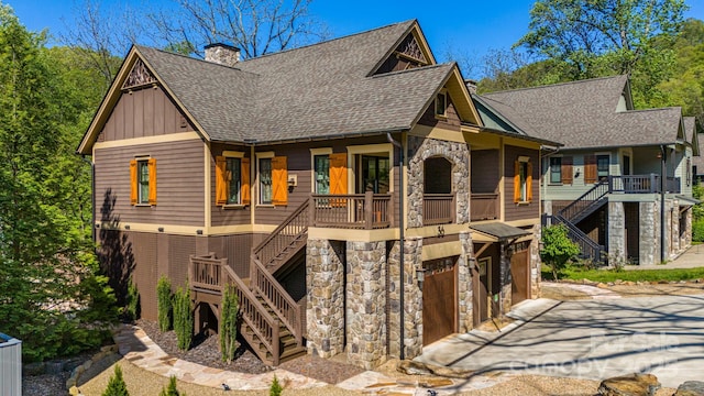 view of front of home with roof with shingles, an attached garage, stairway, and stone siding