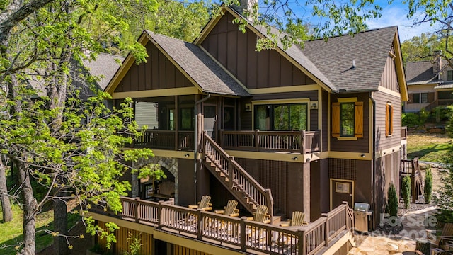 rear view of house featuring board and batten siding, a wooden deck, a shingled roof, and a sunroom