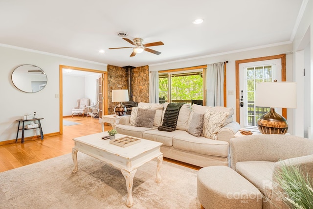 living area featuring ornamental molding, a wood stove, light wood finished floors, and ceiling fan