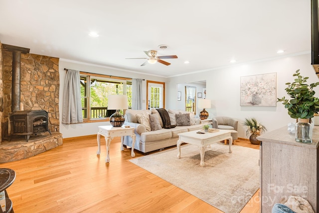 living area featuring crown molding, a wood stove, ceiling fan, and wood finished floors