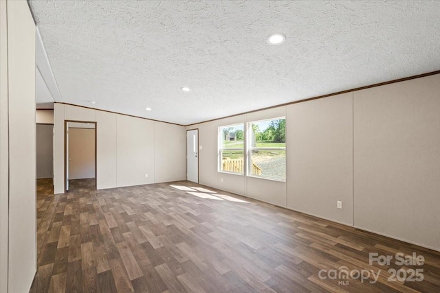 empty room with a decorative wall, ornamental molding, wood finished floors, and a textured ceiling