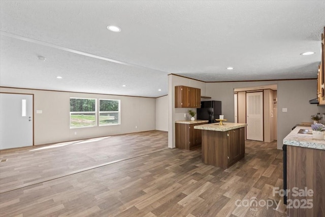 kitchen featuring a center island, open floor plan, light countertops, freestanding refrigerator, and wood finished floors