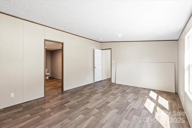 unfurnished bedroom featuring a decorative wall, ornamental molding, wood finished floors, and a textured ceiling