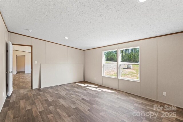 empty room with a decorative wall, a textured ceiling, ornamental molding, and wood finished floors