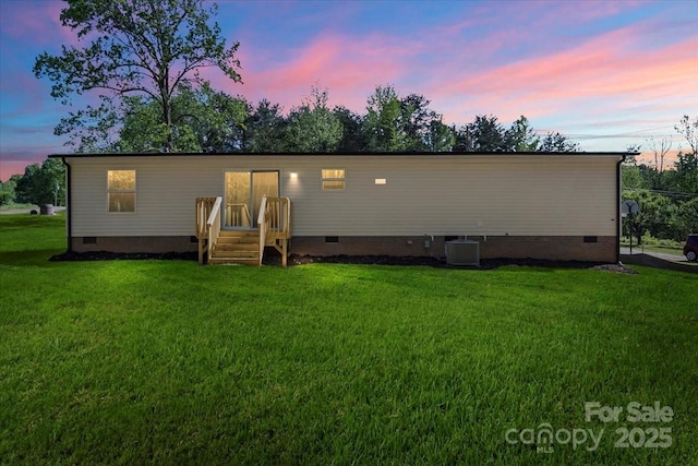 back of property at dusk with a lawn, crawl space, and cooling unit