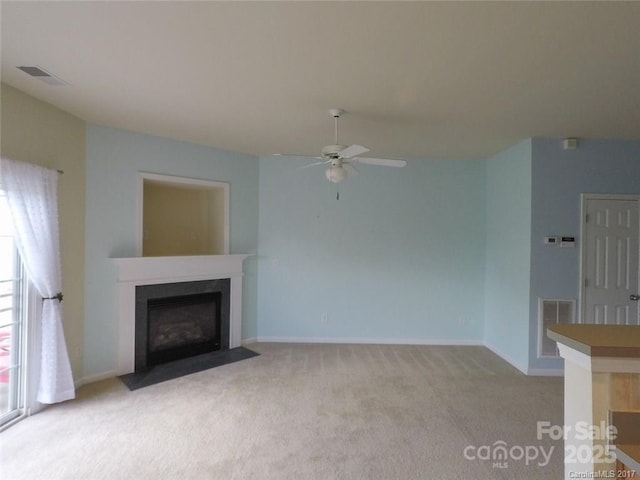 unfurnished living room featuring a fireplace with flush hearth, visible vents, baseboards, light colored carpet, and ceiling fan