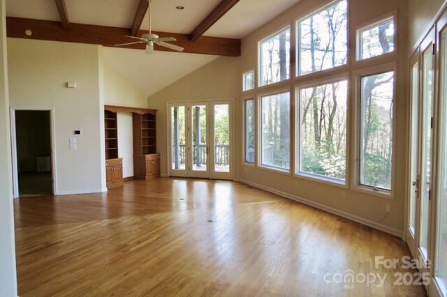 unfurnished living room with ceiling fan, baseboards, beam ceiling, and plenty of natural light