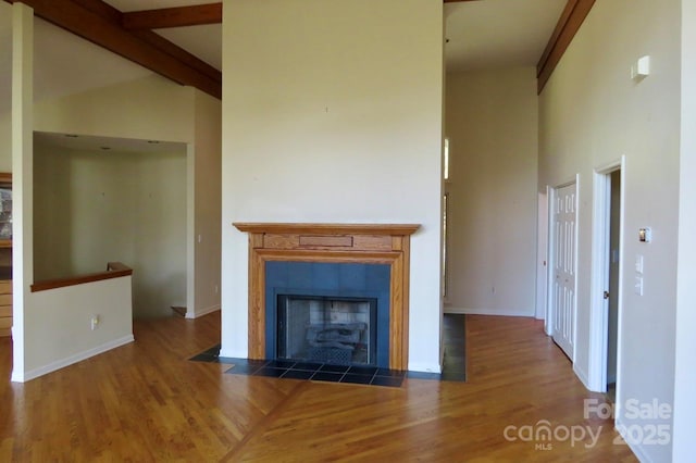 unfurnished living room featuring a tiled fireplace, baseboards, high vaulted ceiling, and wood finished floors