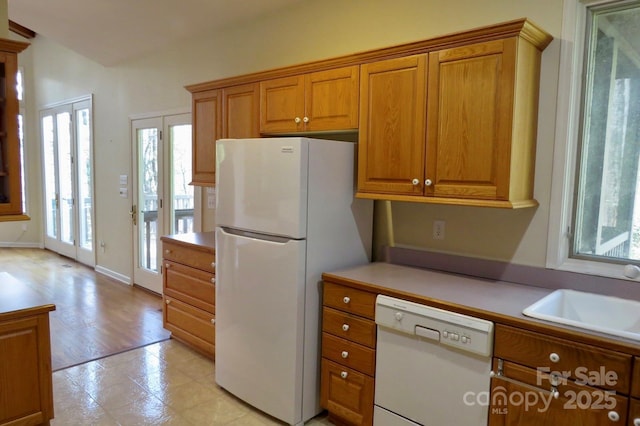 kitchen with brown cabinetry, light countertops, a sink, and white appliances