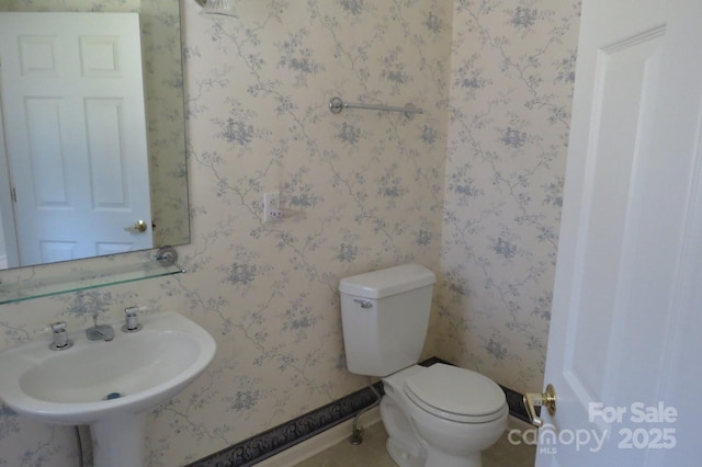 half bath with toilet, a sink, and baseboards