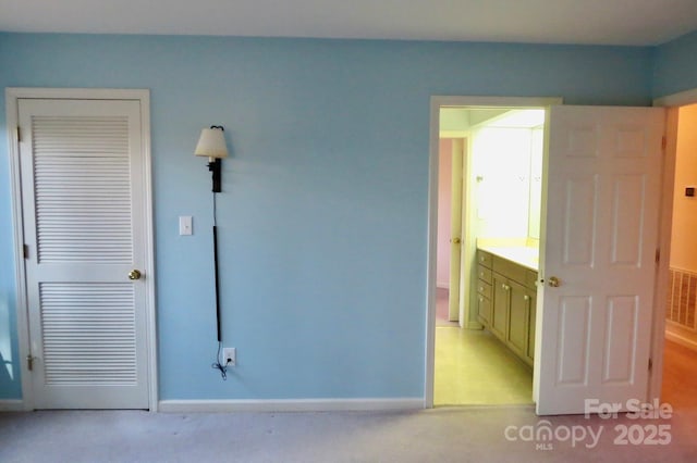 unfurnished bedroom featuring light colored carpet, baseboards, and ensuite bath