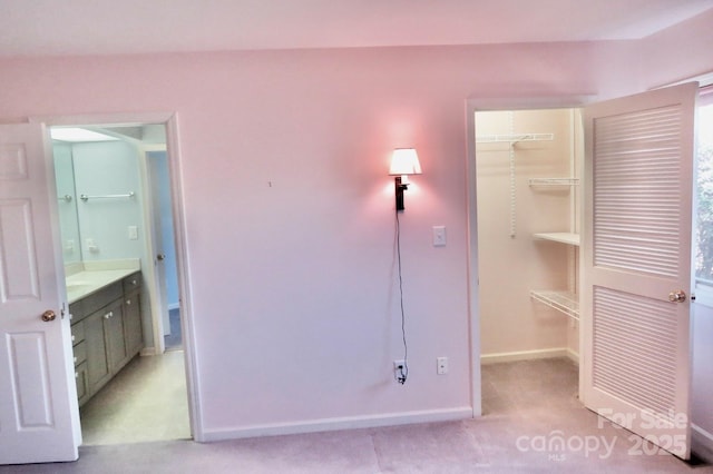 unfurnished bedroom with connected bathroom, a closet, light colored carpet, a spacious closet, and baseboards