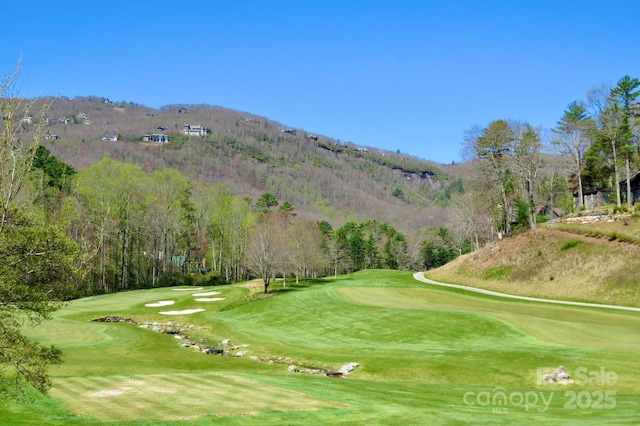 view of property's community with a mountain view, view of golf course, and a lawn