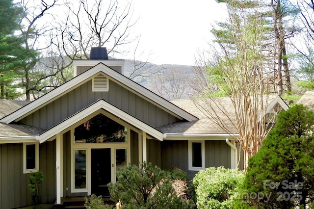 view of front of property with board and batten siding, a chimney, and a shingled roof