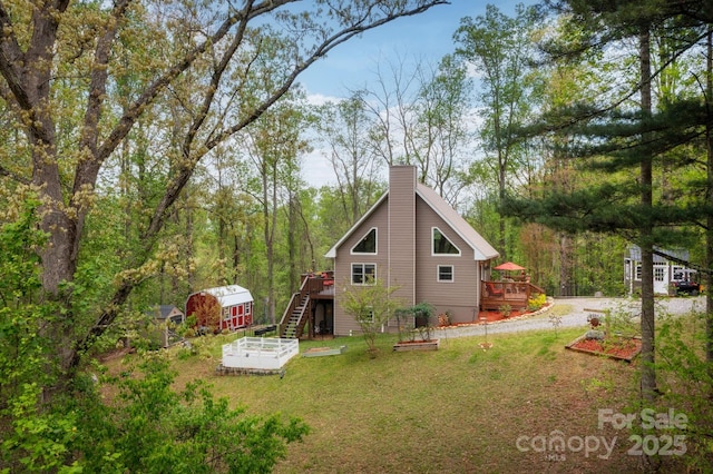 rear view of house with a deck, a vegetable garden, a lawn, an outbuilding, and stairway