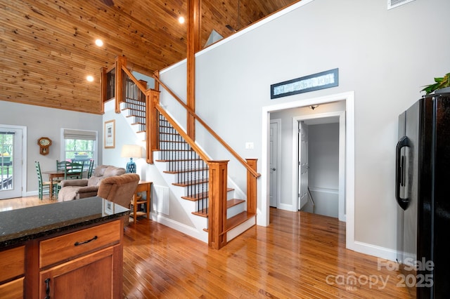 staircase featuring high vaulted ceiling, baseboards, wood ceiling, and hardwood / wood-style floors