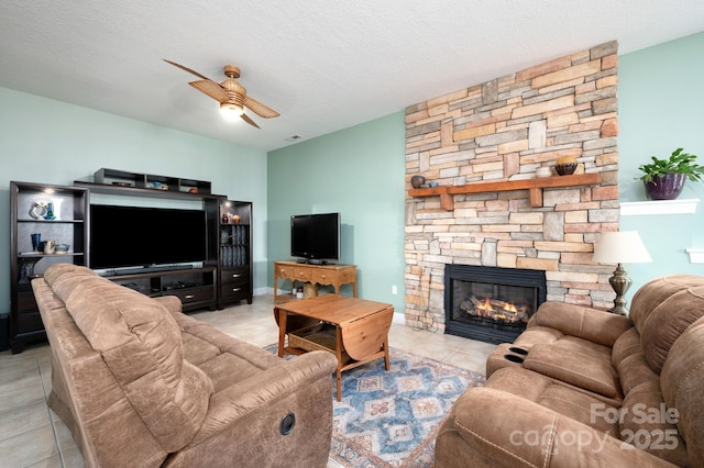 tiled living room with a textured ceiling, ceiling fan, and a fireplace