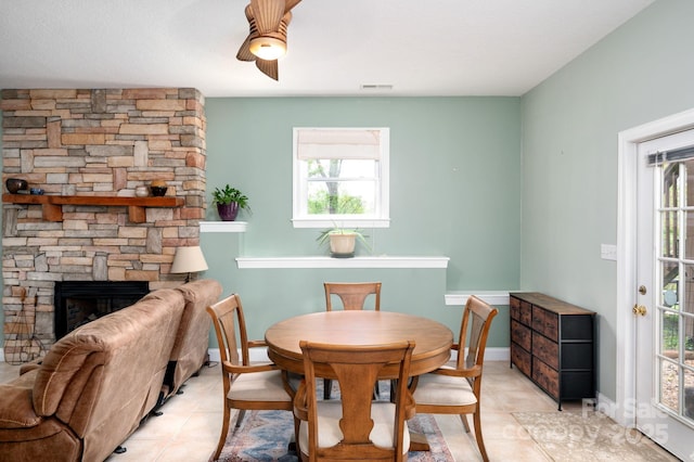 dining room with a stone fireplace, ceiling fan, light tile patterned flooring, and a healthy amount of sunlight