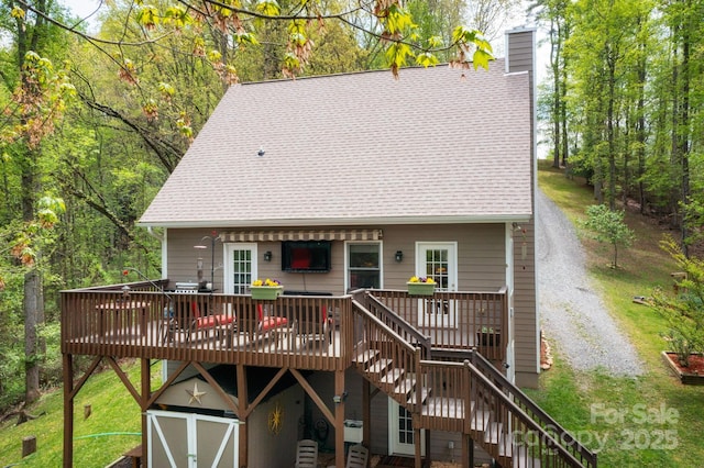 back of property with roof with shingles, a storage shed, a deck, stairway, and a chimney