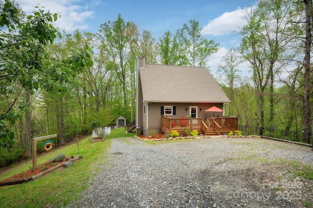view of front of home with a chimney, a deck, an outbuilding, a shed, and gravel driveway