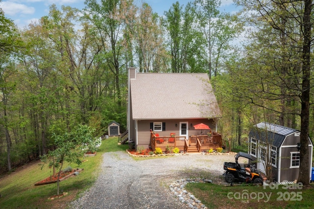 rustic home featuring a storage shed, a wooden deck, an outbuilding, a chimney, and driveway