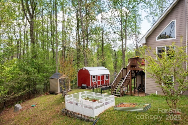 view of yard with stairs, a storage shed, a wooden deck, a vegetable garden, and an outbuilding