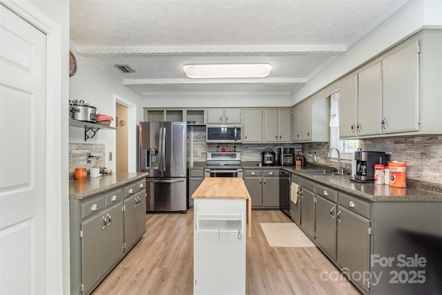 kitchen with gray cabinetry, appliances with stainless steel finishes, a sink, and ornamental molding