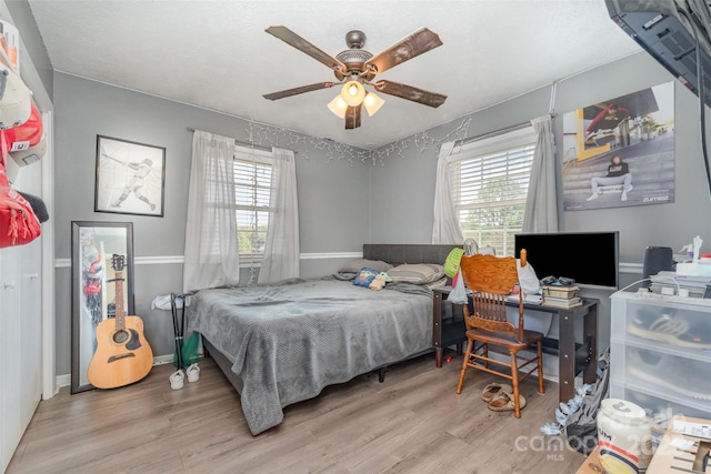 bedroom with a ceiling fan, wood finished floors, baseboards, and multiple windows