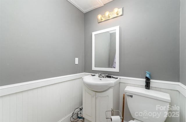 half bathroom featuring vanity, a wainscoted wall, and toilet