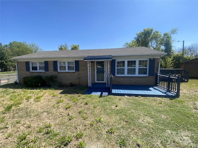 ranch-style house featuring a deck, fence, a front lawn, and brick siding