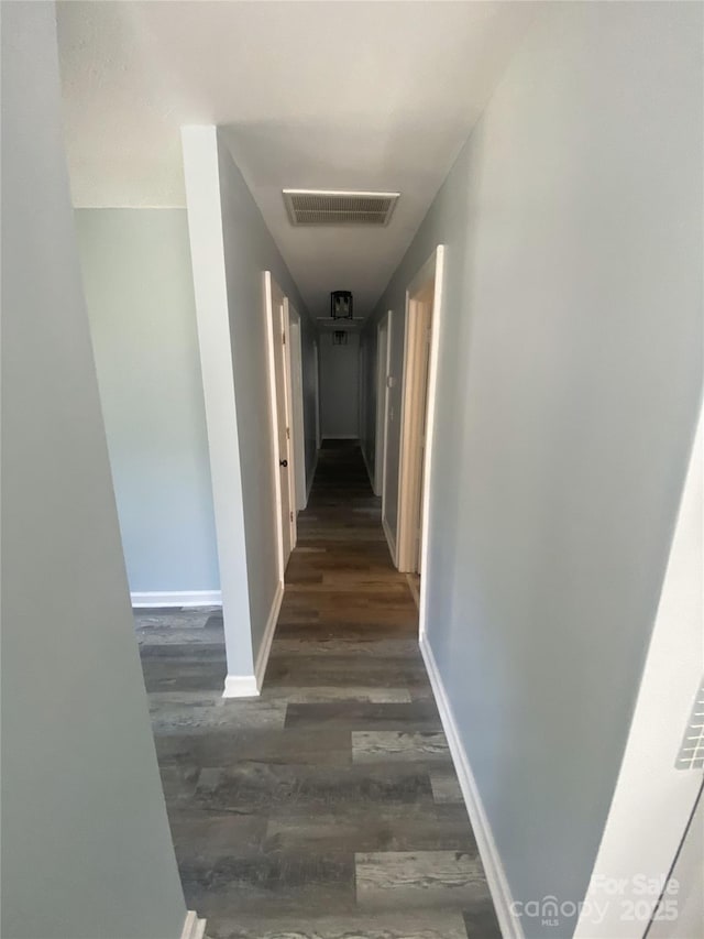 hallway with dark wood-type flooring, visible vents, and baseboards