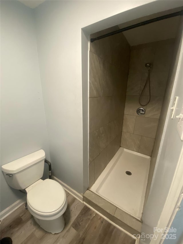 full bath featuring a shower stall, wood finished floors, baseboards, and toilet