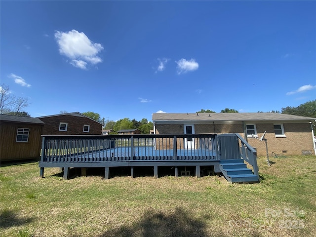 rear view of house featuring crawl space, brick siding, a deck, and a lawn