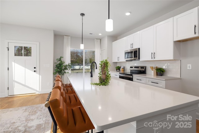 kitchen featuring light countertops, light wood-type flooring, an island with sink, stainless steel appliances, and backsplash