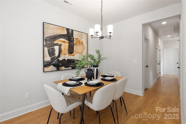 dining room featuring a notable chandelier, baseboards, attic access, visible vents, and light wood finished floors