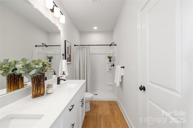 bathroom with curtained shower, a sink, toilet, double vanity, and wood finished floors