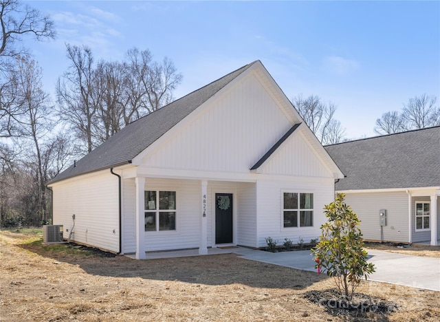 modern farmhouse style home featuring a shingled roof, cooling unit, and covered porch