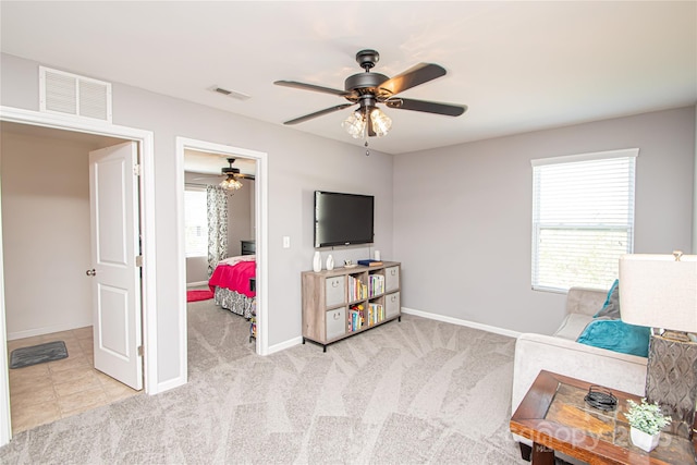 living area with light carpet, visible vents, baseboards, and a ceiling fan