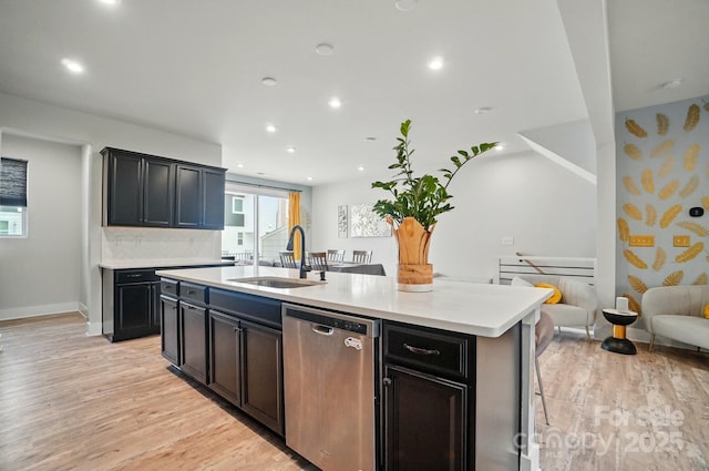 kitchen featuring stainless steel dishwasher, a sink, a center island with sink, and light wood-type flooring