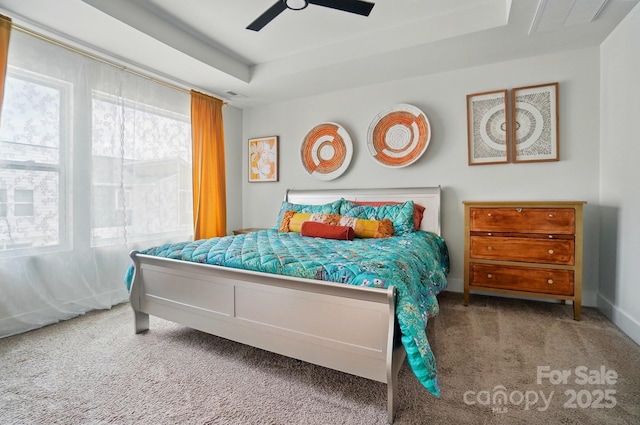 carpeted bedroom with a raised ceiling and ceiling fan