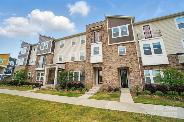 townhome / multi-family property featuring board and batten siding, stone siding, and a front yard