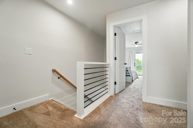 hall with carpet floors, attic access, baseboards, and an upstairs landing