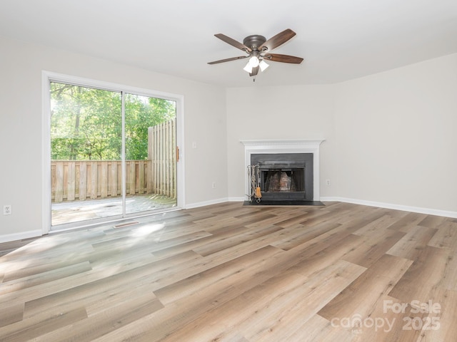 unfurnished living room with ceiling fan, wood finished floors, a fireplace with flush hearth, and baseboards