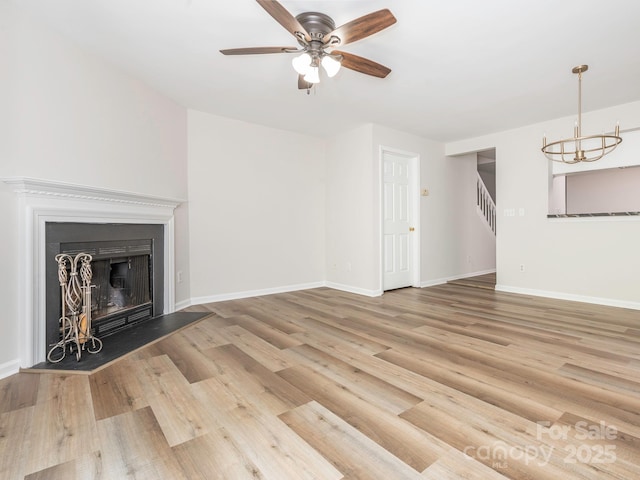 unfurnished living room with baseboards, a fireplace, stairs, ceiling fan with notable chandelier, and wood finished floors