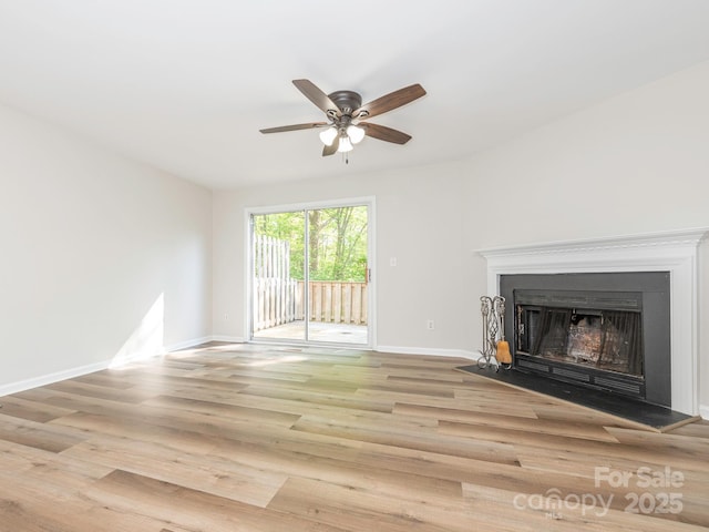 unfurnished living room with wood finished floors, ceiling fan, baseboards, and a fireplace with raised hearth