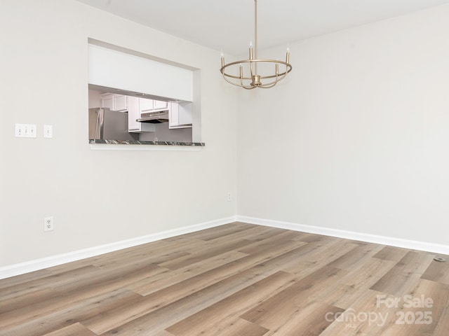 unfurnished dining area with wood finished floors, a notable chandelier, and baseboards