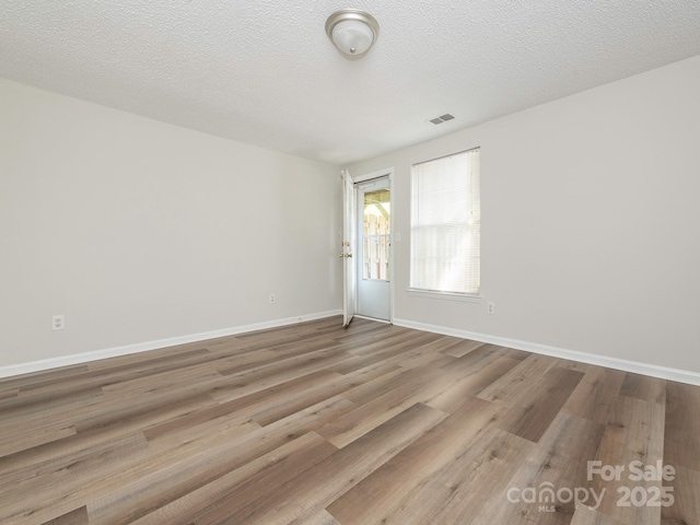 empty room featuring a textured ceiling, wood finished floors, baseboards, and visible vents